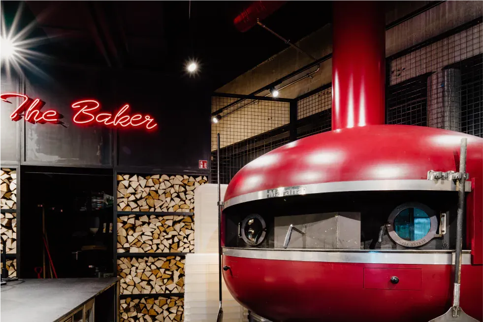Roter Holzofen unter der Leuchtschrift „The Baker“